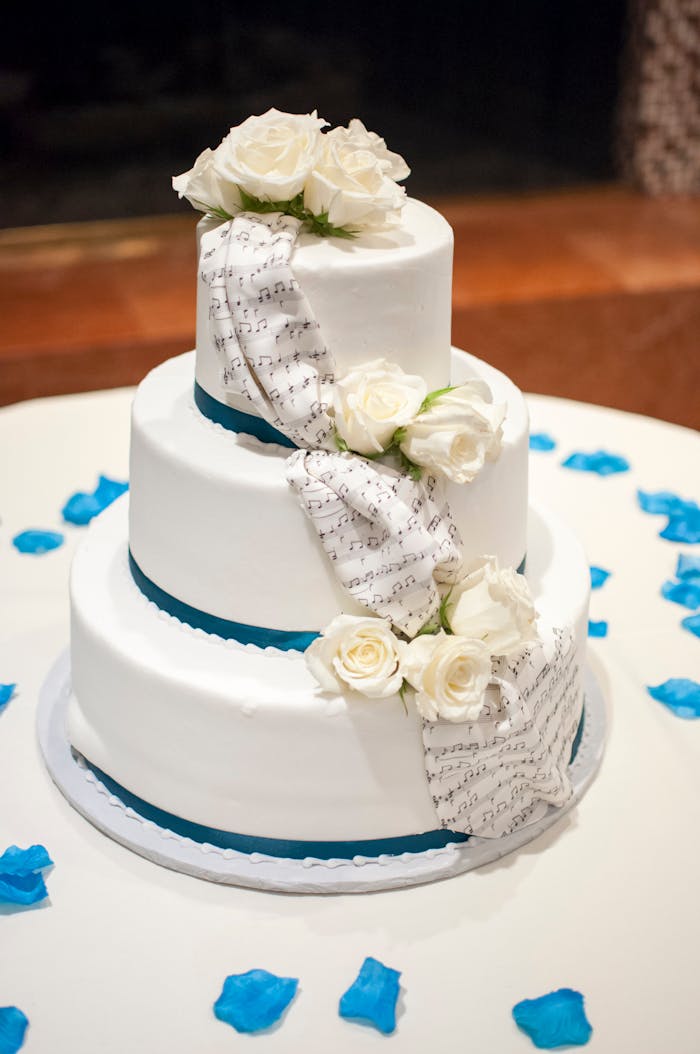 Three-tier wedding cake with white roses and musical notes. Elegant design for special occasions.